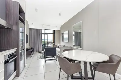 a kitchen and living room with a table and chairs at Menlyn Main Apartments Trilogy Collection in Pretoria