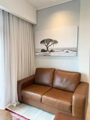 a brown leather couch in a living room with a tree at Menlyn Maine Trilogy Apartments When Home is Far in Pretoria