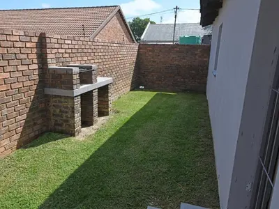a small backyard with a brick wall and grass at Soliha Guesthouse in Trichardt