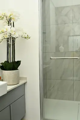 a glass shower door in a bathroom with a vase of flowers at Apartment in Menlyn Maine, The Capital Trilogy in Pretoria