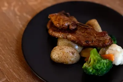 a black plate of food with meat potatoes and broccoli at Zebras Crossing in Modimolle