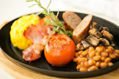 a black plate of food with eggs bacon tomatoes and beans at Mavuta Boutique Apartments in Polokwane