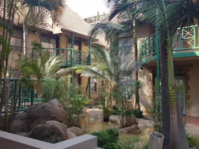 a building with palm trees and a pond in front of it at Court Classique Suite Hotel in Pretoria