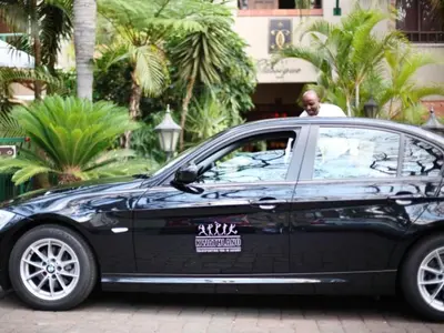 a man is standing next to a black car at Court Classique Suite Hotel in Pretoria