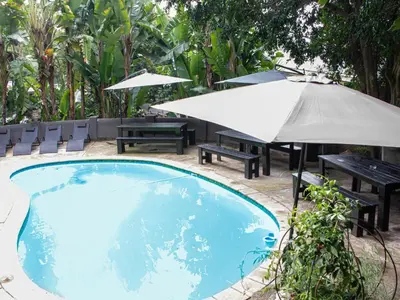 a swimming pool with a table and umbrella and benches at Muckleneuk Manor in Pretoria