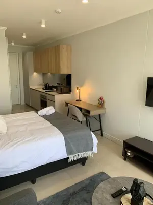 a bedroom with a bed and a desk and a kitchen at Ellipse Luxurious Tamarind Green Studio Experience in Midrand