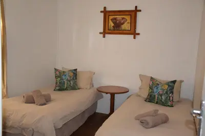 two beds in a room with a table and a picture on the wall at Trout Ways in Waterval Boven