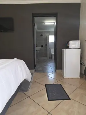 a bedroom with a bed and a bathroom with a refrigerator at The Good Samaritan 4 in Witbank