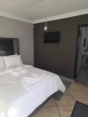 a bedroom with a white bed with a tv on the wall at The Good Samaritan 4 in Witbank