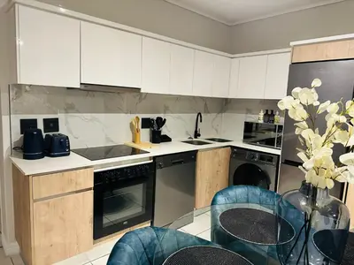 a kitchen with white cabinets and a glass table at Kaso holidays in Pretoria