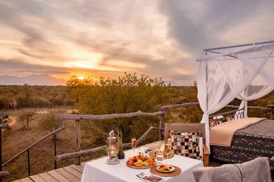 a table and chairs on a deck with a view of the wilderness at Kapama Karula in Kapama Private Game Reserve