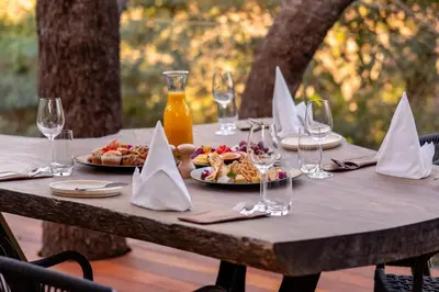 a wooden table with plates of food and wine glasses at Kapama Karula in Kapama Private Game Reserve