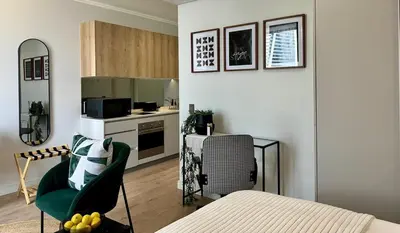 a living room with a green chair and a kitchen at Explore Ellipse - The Sage Apartment in Midrand