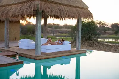 a woman laying on a bed next to a pool at Kapama River Lodge in Kapama Private Game Reserve