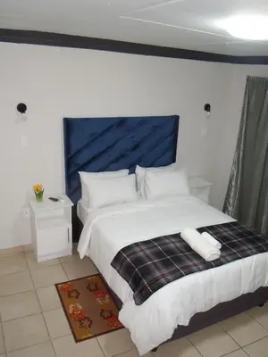 a bedroom with a large white bed with a blue headboard at Daeka Guesthouse in Kempton Park