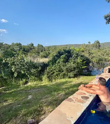 a man sitting on a wall in a swimming pool at Private African Retreat at 3000ha Mangweni Game Reserve in Elandsbosch