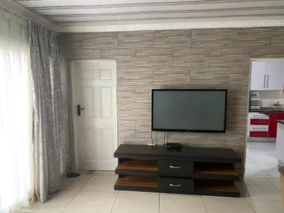 a living room with a flat screen tv on a brick wall at XNZN Guest House in Tzaneen