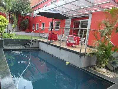 a swimming pool in front of a red house at Red Square Home in Pretoria