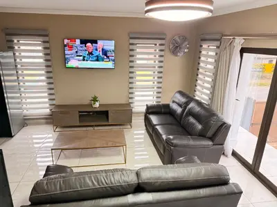 a living room with a leather couch and a tv at Dunamis Lodge in Giyani