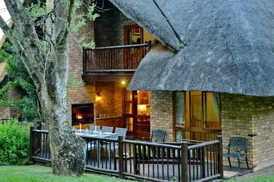 a house with a thatch roof with chairs and a porch at Cambalala - Luxury Units - in Kruger Park Lodge - Serviced Daily, Free Wi-Fi in Hazyview