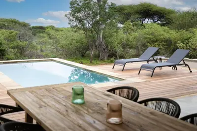 a deck with a table and chairs and a swimming pool at Villa Kolobe in Hoedspruit
