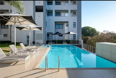 a swimming pool with chairs and umbrellas on a building at Luxurious queen room in Pretoria