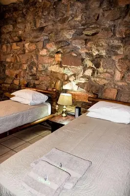 a bedroom with two beds and a stone wall at Tumuga Game Ranches