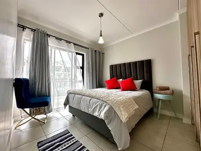 a bedroom with a bed with red pillows and a window at The Blyde - 3 Bedroom Lagoon Facing Luxury Apartment in Pretoria