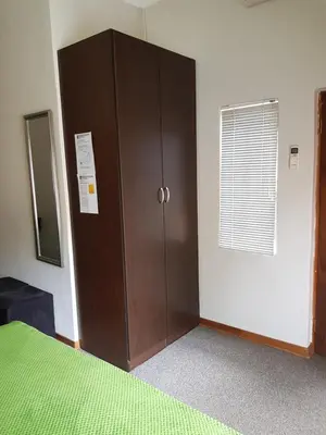a bedroom with a brown cabinet and a green bed at Sekelbos Guesthouse in Pretoria