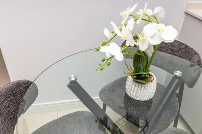 a glass table with a vase with white flowers in it at RestHaus Suite, Ellipse Waterfall in Midrand