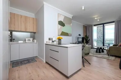 a kitchen with white cabinets and a living room at Ellips Smartz Apartment in Midrand