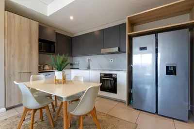 a kitchen with a table and chairs and a refrigerator at #AlimamaSpaces Koki's Place Menlyn in Pretoria