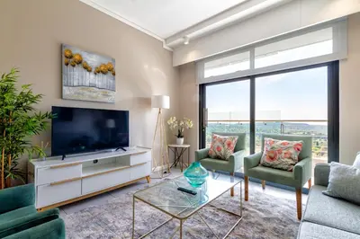 a living room with a flat screen tv and green chairs at #AlimamaSpaces Koki's Place Menlyn in Pretoria