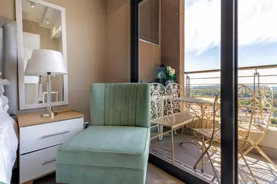 a bedroom with a green chair and a balcony at #AlimamaSpaces Koki's Place Menlyn in Pretoria
