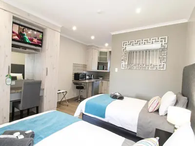 a hotel room with two beds and a desk at De Stroom Studio Apartments in Secunda