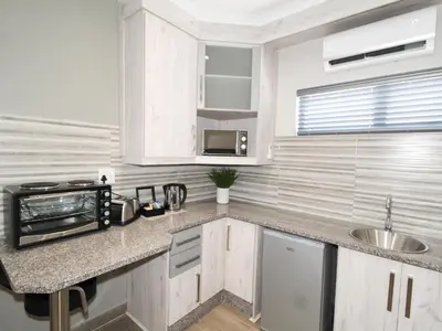 a white kitchen with a microwave and a sink at De Stroom Studio Apartments in Secunda