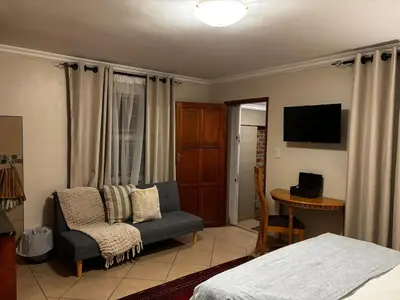 a bedroom with a bed and a chair and a television at Olivestay at Olympus - Studio Apartment in Pretoria