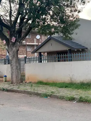 a brick building with a fence and a tree at Madlabeezy in Kempton Park