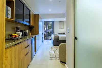 a kitchen with wooden cabinets and a bed in a room at #AlimamaSpaces Manson's Menlyn Maine in Pretoria