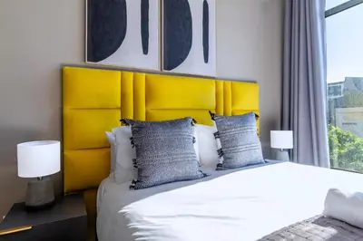 a bed with a yellow headboard in a bedroom at #AlimamaSpaces Chelsea's Menlyn Maine in Pretoria