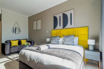 a bedroom with a large bed with a yellow headboard at #AlimamaSpaces Chelsea's Menlyn Maine in Pretoria