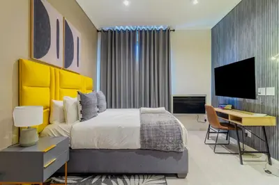 a bedroom with a bed and a desk and a television at #AlimamaSpaces Chelsea's Menlyn Maine in Pretoria