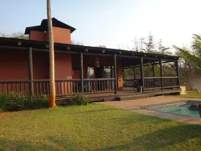 a red house with a porch and a pool at Hazyview Country Estate in Swartfontein