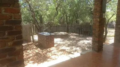 a patio with a table and a fence and trees at Bush Babies Cottage in Marloth Park