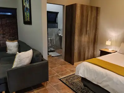a bedroom with a bed and a couch next to a room at Cozy Corner Cottage near wilgers hospital & Menlyn in Pretoria