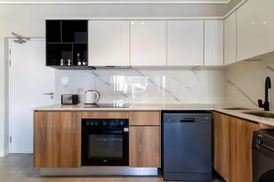 a kitchen with white cabinets and a black dishwasher at #AlimamaSpaces The Rob's Munyaka in Midrand