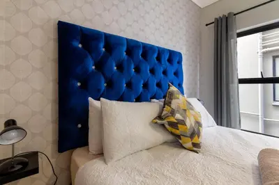 a bed with a blue padded headboard in a bedroom at #AlimamaSpaces The Rob's Munyaka in Midrand