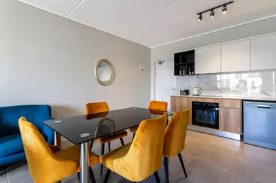 a kitchen and dining room with a table and yellow chairs at #AlimamaSpaces The Rob's Munyaka in Midrand