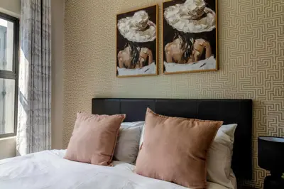 a bedroom with a bed with three paintings on the wall at #AlimamaSpaces The Manson's Heights in Midrand