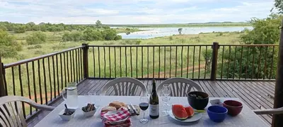 a table with a bottle of wine and fruit on a balcony at Vaalkop Dam Reserve, self-catering log cabin holiday home in Beestekraal, South Africa in Beestekraal